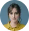 Portrait of a young woman with dark hair wearing a mustard yellow top against a blue background.